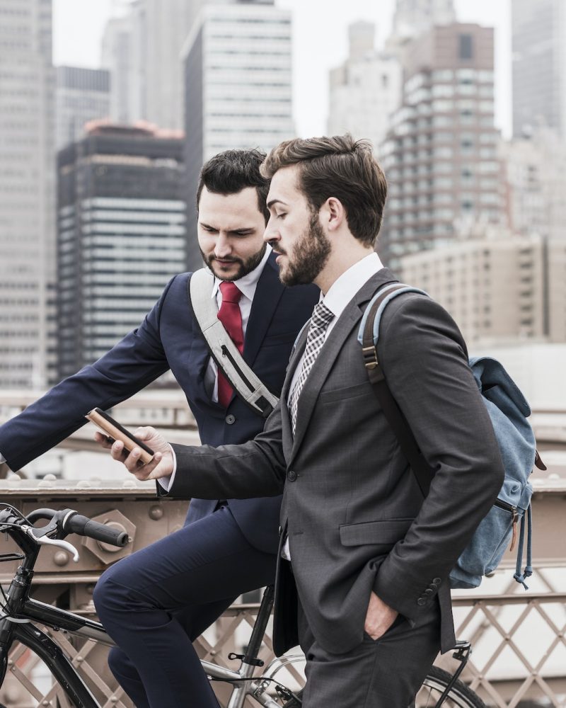 USA, New York City, two businessmen with bicycle and cell phone on Brooklyn Bridge